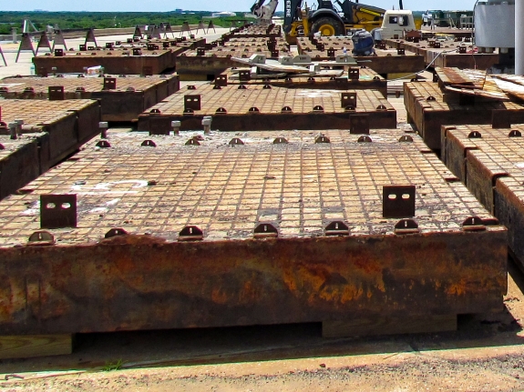 Medium-format photograph: Pad Deck, Launch Complex 39-B, east side of Flame Trench. Removed Crawlerway Grid Panels lie stacked on cribbing. Note the temporary lifting lugs (edge-up, with 2 holes in each one of them for the attachment of lifting hardware) which were welded to the top flanges of the Mystery I-Beams on every Panel, and which were used for Panel lifting operations because the original Ring Bars recessed into the Panel surfaces were corroded beyond any useful degree of trustworthiness and could not be used. Photo credit: Withheld by request.